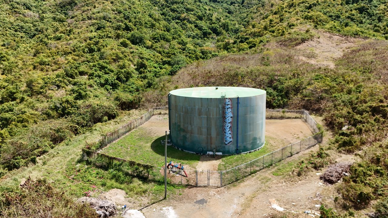 Drone shot of a water storage tank surrounded by greenery on a hillside.